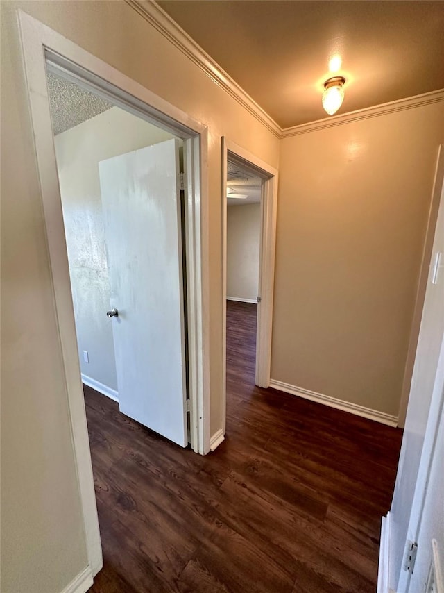 hallway featuring dark wood finished floors, baseboards, and crown molding