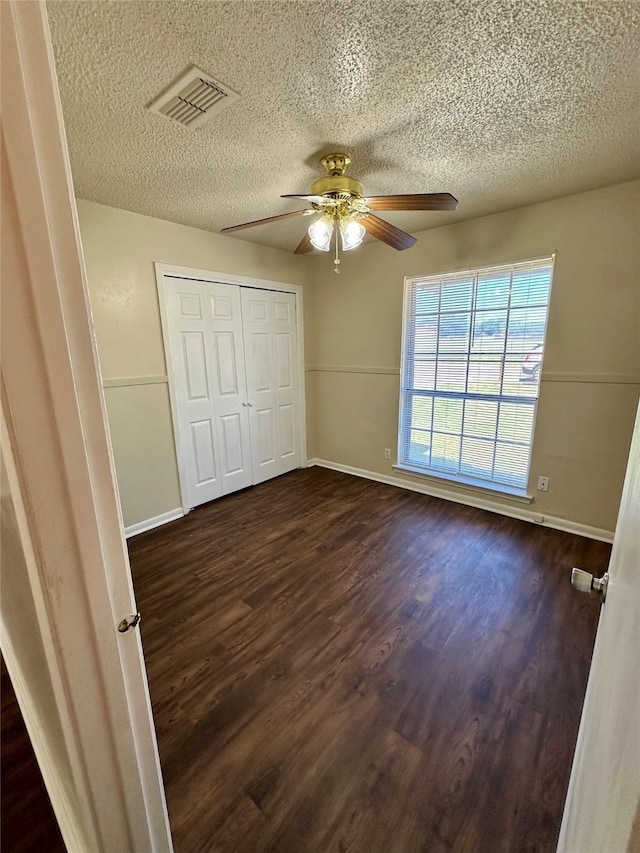 unfurnished bedroom featuring baseboards, visible vents, a textured ceiling, and dark wood finished floors