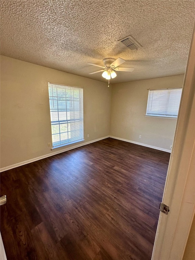 empty room with dark wood-style floors, a ceiling fan, visible vents, baseboards, and a textured ceiling