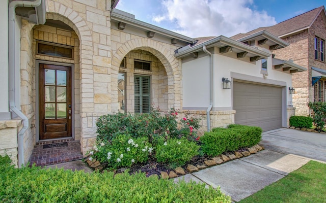 entrance to property with stucco siding, driveway, an attached garage, and stone siding