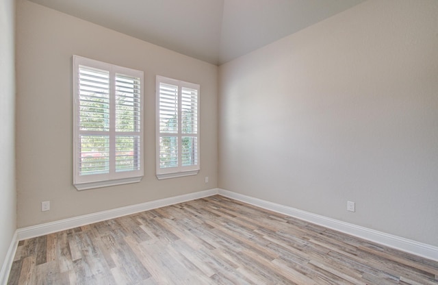 empty room featuring light wood-style floors, vaulted ceiling, and baseboards