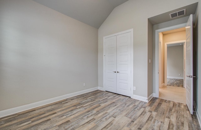 unfurnished bedroom with wood finished floors, a closet, baseboards, visible vents, and lofted ceiling