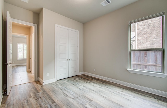 unfurnished bedroom with wood finished floors, visible vents, baseboards, and a closet
