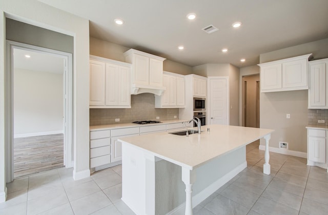 kitchen featuring decorative backsplash, a sink, appliances with stainless steel finishes, visible vents, and a kitchen island with sink