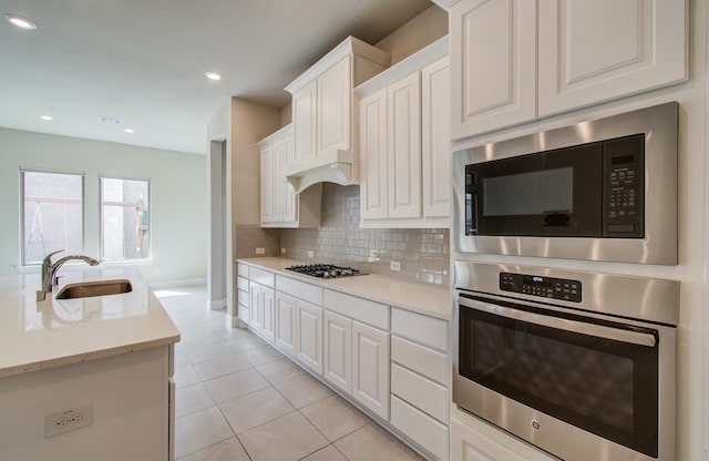 kitchen featuring decorative backsplash, appliances with stainless steel finishes, white cabinets, a sink, and light tile patterned flooring