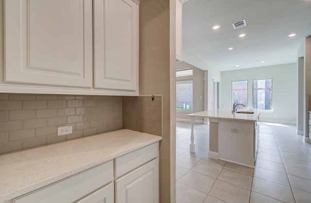 kitchen featuring light tile patterned floors, white cabinetry, a sink, visible vents, and backsplash