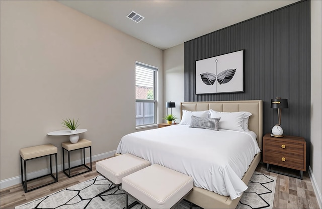 bedroom featuring baseboards, light wood-type flooring, visible vents, and an accent wall