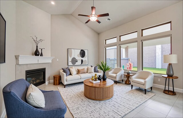 tiled living area featuring high vaulted ceiling, ceiling fan, a glass covered fireplace, visible vents, and baseboards