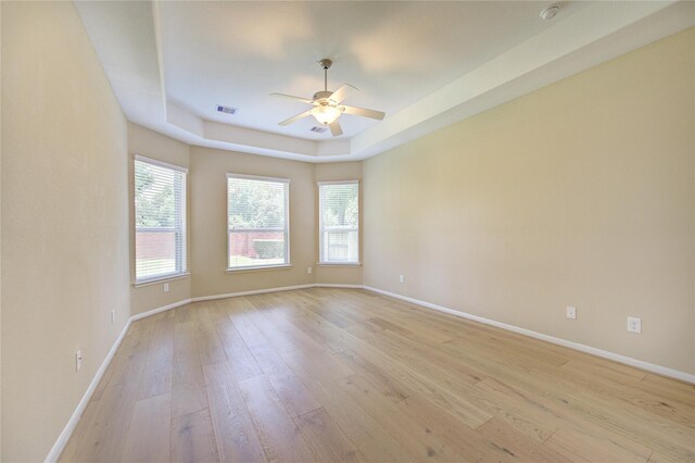 empty room featuring light wood finished floors, a ceiling fan, baseboards, and a tray ceiling