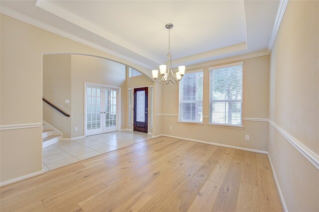 empty room with french doors, a chandelier, stairs, a raised ceiling, and wood finished floors