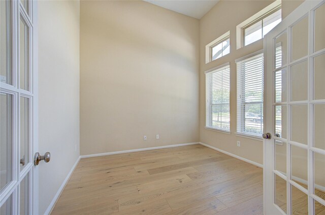 empty room with light wood finished floors, healthy amount of natural light, french doors, and baseboards