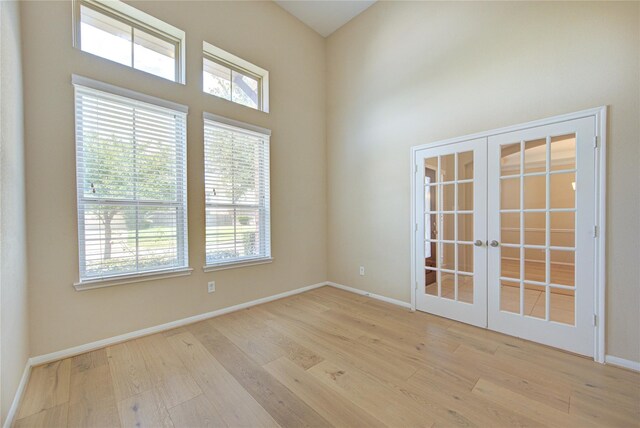 unfurnished room with healthy amount of natural light, wood finished floors, french doors, and a towering ceiling