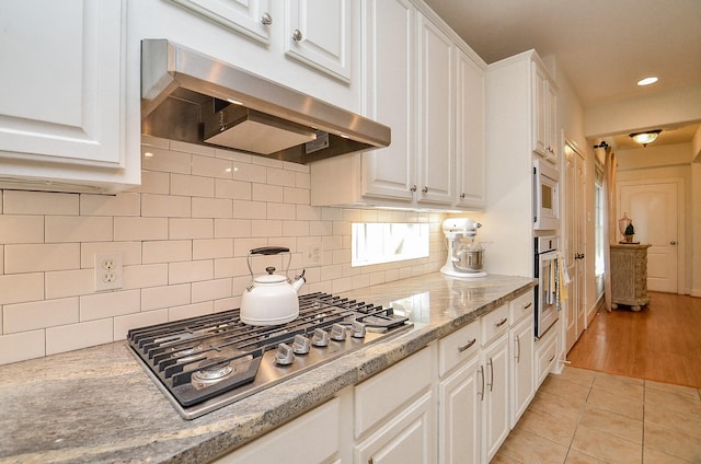 1615 Lakeside Enclave Dr, Houston, TX 77077 - kitchen featuring appliances with stainless steel finishes, under cabinet range hood, white cabinetry, light tile patterned floors, and decorative backsplash