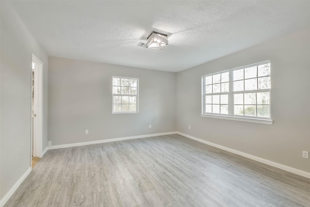 empty room with a textured ceiling, light wood finished floors, and baseboards