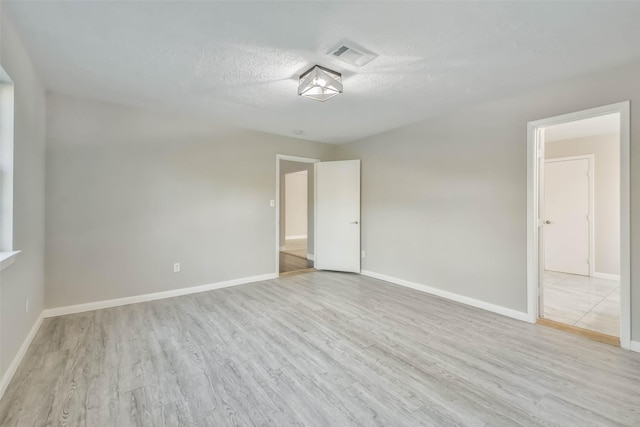 empty room with a textured ceiling, visible vents, wood finished floors, and baseboards