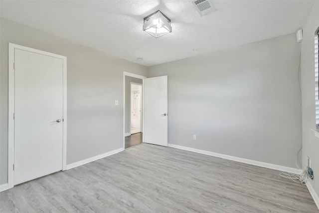 unfurnished bedroom with a textured ceiling, visible vents, wood finished floors, and baseboards