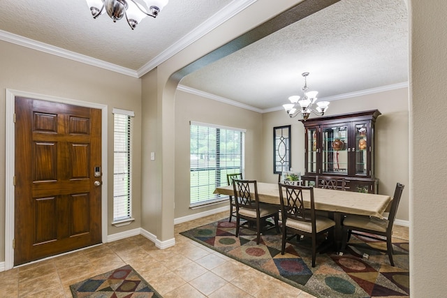 tiled foyer entrance featuring an inviting chandelier, a textured ceiling, baseboards, ornamental molding, and arched walkways