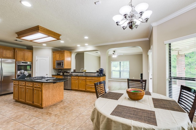 kitchen featuring arched walkways, light tile patterned floors, stainless steel appliances, a kitchen island, and dark countertops