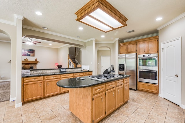 kitchen featuring light tile patterned floors, visible vents, a kitchen island, arched walkways, and appliances with stainless steel finishes