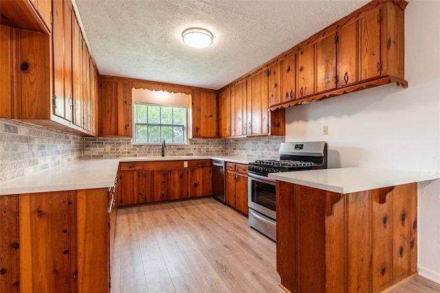 kitchen featuring a textured ceiling, brown cabinets, a sink, appliances with stainless steel finishes, and light wood-style floors