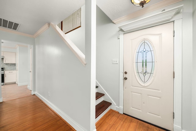 foyer featuring crown molding, stairs, visible vents, light wood-style flooring, and baseboards