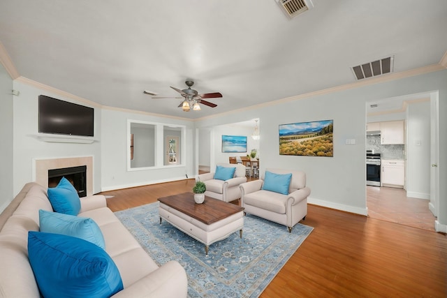 living area with light wood finished floors, visible vents, a ceiling fan, and ornamental molding
