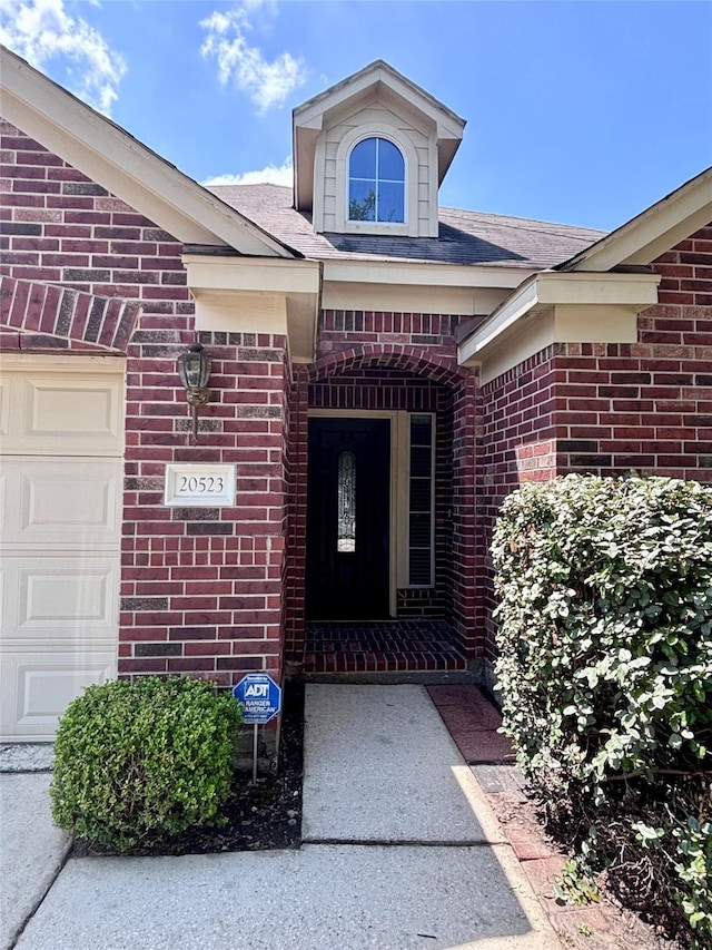 entrance to property featuring a shingled roof, brick siding, and a garage