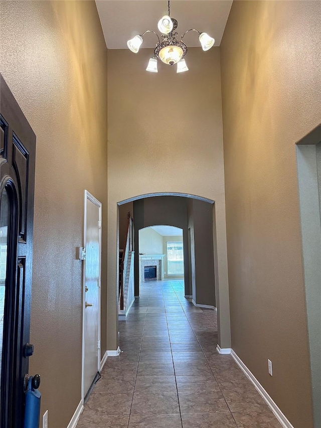 hall with baseboards, arched walkways, an inviting chandelier, and a towering ceiling