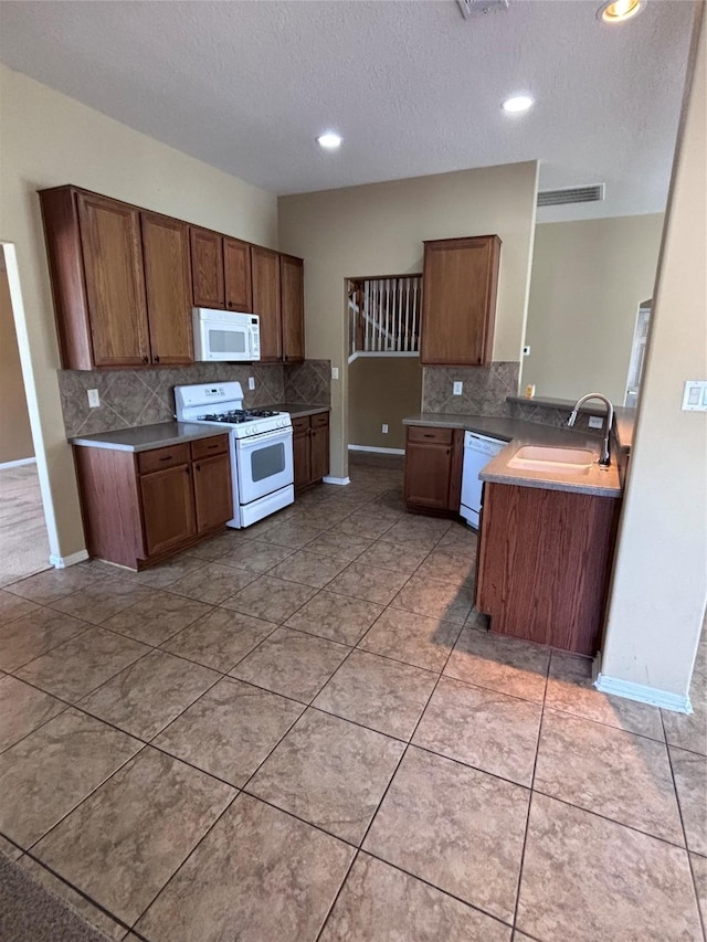 kitchen with tasteful backsplash, white appliances, brown cabinetry, and a sink