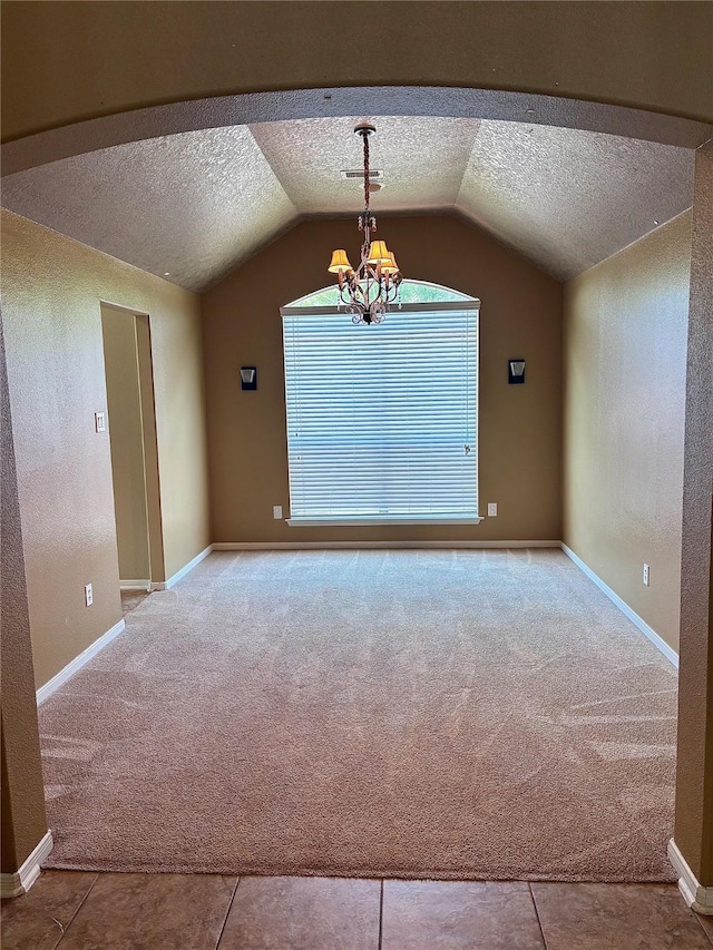 carpeted spare room featuring a textured ceiling, vaulted ceiling, a chandelier, and baseboards