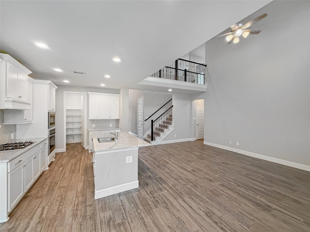 kitchen with decorative backsplash, a sink, ceiling fan, baseboards, and stainless steel gas cooktop