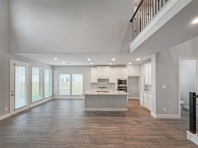 kitchen featuring a towering ceiling, white cabinets, a kitchen island with sink, and open floor plan
