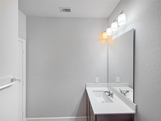 bathroom with baseboards, visible vents, a textured wall, and vanity