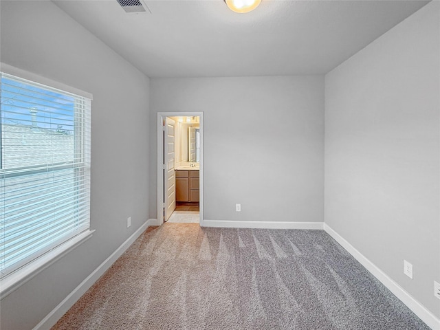 unfurnished bedroom featuring baseboards, visible vents, light carpet, and connected bathroom