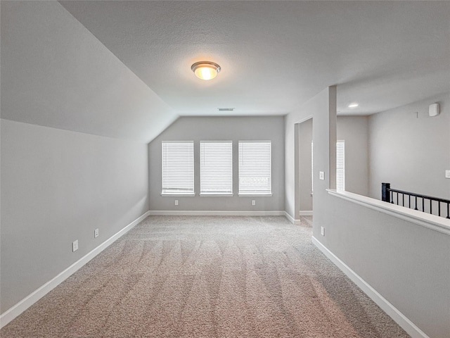 additional living space featuring baseboards, visible vents, carpet, and vaulted ceiling