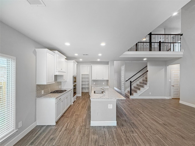 kitchen featuring wood finished floors, decorative backsplash, appliances with stainless steel finishes, a sink, and baseboards