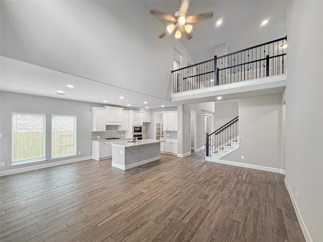 unfurnished living room featuring wood finished floors, baseboards, stairway, a ceiling fan, and a high ceiling