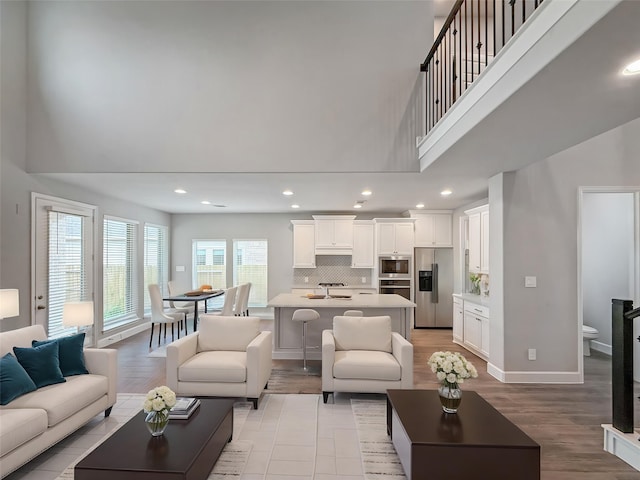 living area with recessed lighting, light wood finished floors, baseboards, and a high ceiling