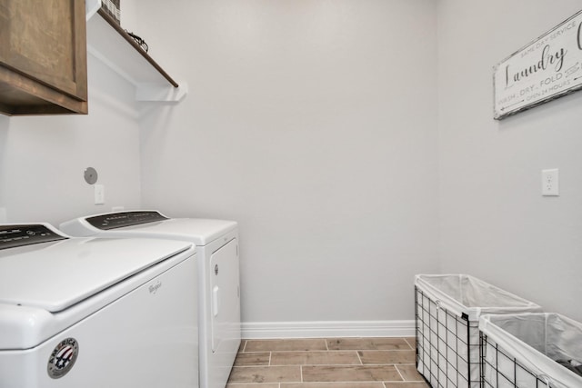 washroom featuring baseboards, wood tiled floor, cabinet space, and washing machine and clothes dryer