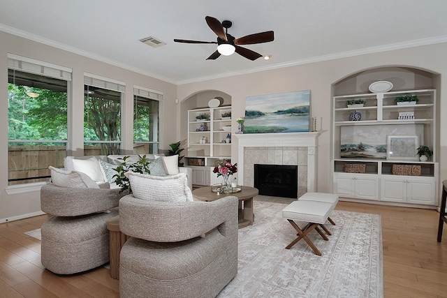 living room featuring a ceiling fan, light wood-style flooring, built in shelves, ornamental molding, and a fireplace