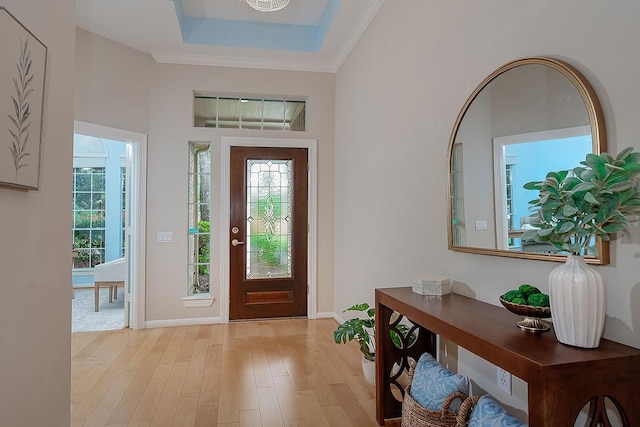 foyer with light wood-style floors, a raised ceiling, and baseboards