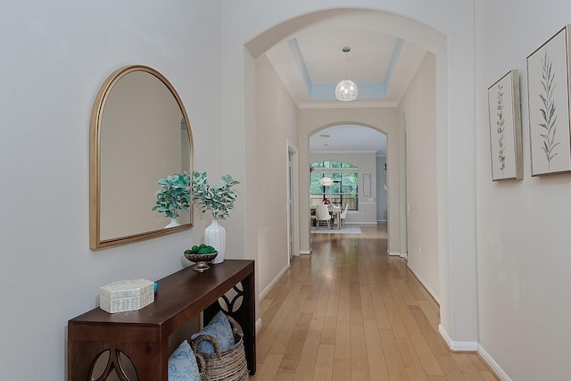 corridor with arched walkways, baseboards, light wood finished floors, and a tray ceiling