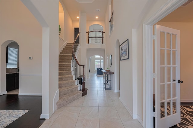 foyer with arched walkways, stairway, baseboards, a high ceiling, and recessed lighting