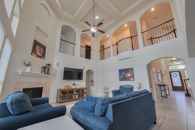 living room with a stone fireplace, a ceiling fan, a towering ceiling, beamed ceiling, and coffered ceiling