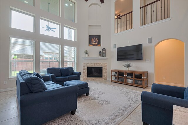 living room with a ceiling fan, a stone fireplace, visible vents, a towering ceiling, and arched walkways