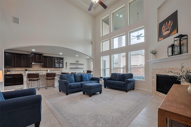 living room with a fireplace, ceiling fan, high vaulted ceiling, arched walkways, and light tile patterned floors