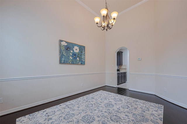 empty room featuring arched walkways, baseboards, dark wood-style floors, a chandelier, and ornamental molding