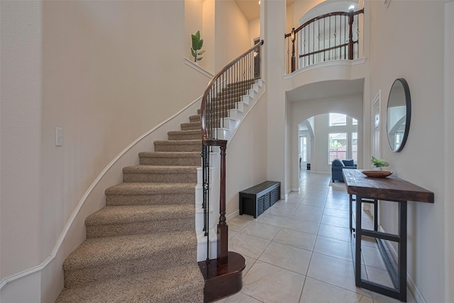 foyer entrance with arched walkways, a high ceiling, light tile patterned floors, and stairway