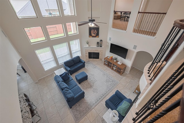 tiled living area featuring a ceiling fan, a towering ceiling, a tiled fireplace, arched walkways, and baseboards