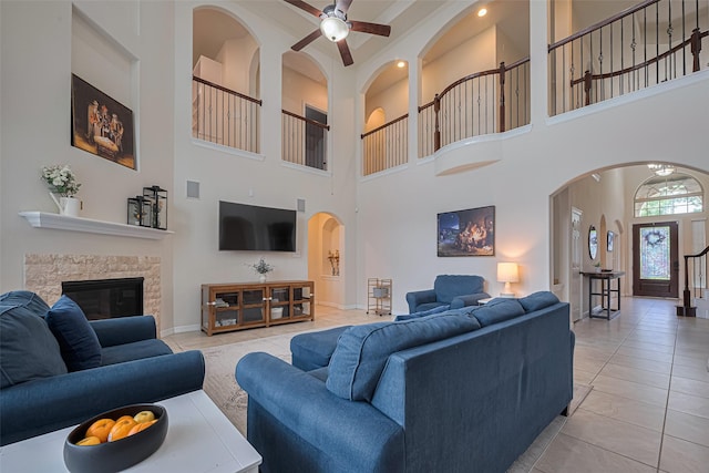 living area featuring a ceiling fan, a towering ceiling, a fireplace, arched walkways, and light tile patterned floors